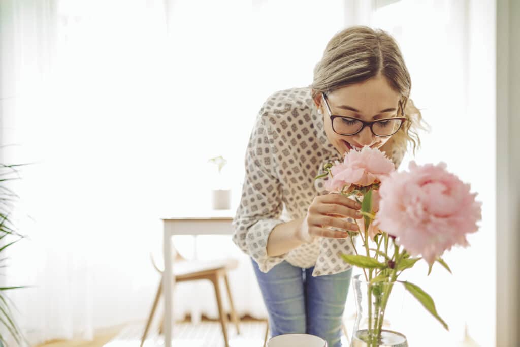 Kvinne med briller og blondt hår smiler og lukter på blomster, brukt for å illustrere hvordan du kan gjøre boligen lettere å selge med riktig styling.